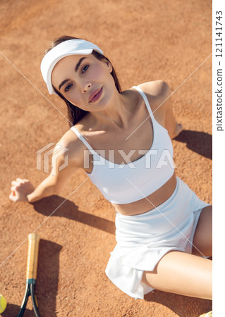 Pretty young tennis player in white clothes sitting on the tennis courts 121141743