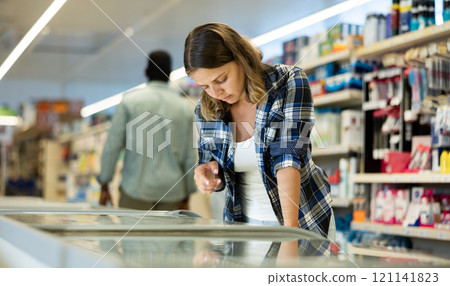 Woman standing at refrigerator in supermarket, choosing frozen food 121141823