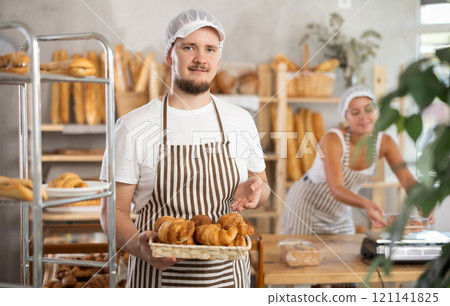 Young salesman displays croissants in square wicker basket 121141825