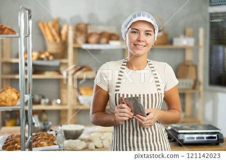 Young baker girl is standing near work table in kitchen, working with dough Young baker girl is standing near work table in kitchen, working with dough 121142023