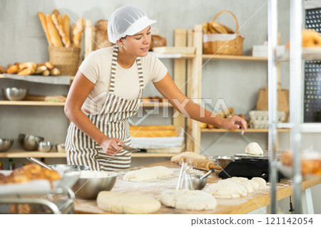 Girl baker cut small pieces of dough from large lump and put them on scales. 121142054