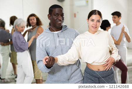 Happy african-american guy and caucasian girl practising paired latin dance in dance studio 121142088