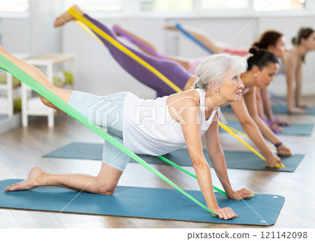 Aged woman exercising with elastic band during group fitness class 121142098