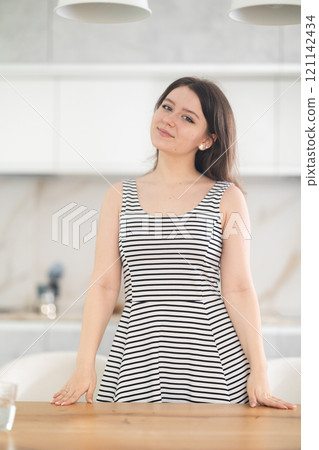 Smiling young woman standing at table 121142434