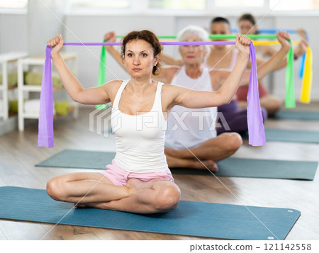 Woman using exercise band at group training in fitness studio 121142558