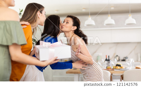 Joyful woman giving greeting kiss to bestie at home party Joyful woman giving greeting kiss to bestie at home party 121142576