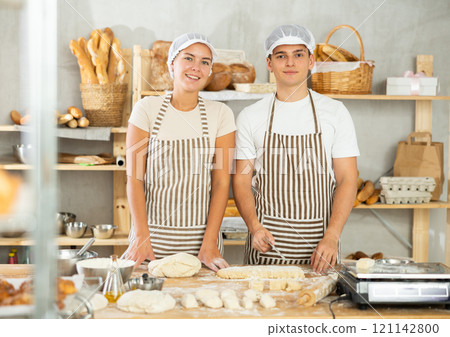 Girl and guy bakers cut small pieces of dough from large lump and put them on scales. Girl and guy bakers cut small pieces of dough from large lump and put them on scales. 121142800