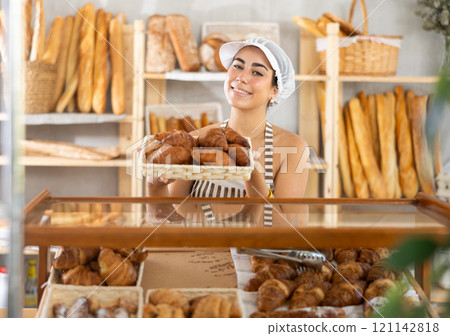 Young saleswoman displays croissants in square wicker basket 121142818