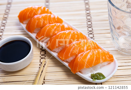 Blue rectangular ceramic plate of delicious salmon nigiri with soy souse on bamboo mat. 121142855