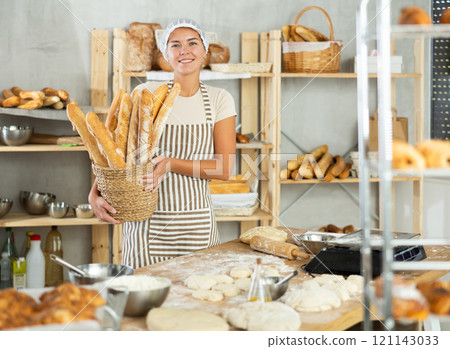 Smiling female baker presenting fresh baguettes in bakery Smiling female baker presenting fresh baguettes in bakery 121143033