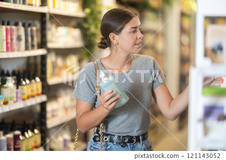Positive young girl purchaser choosing cosmetic product in large supermarket Positive young girl purchaser choosing cosmetic product in large supermarket 121143052