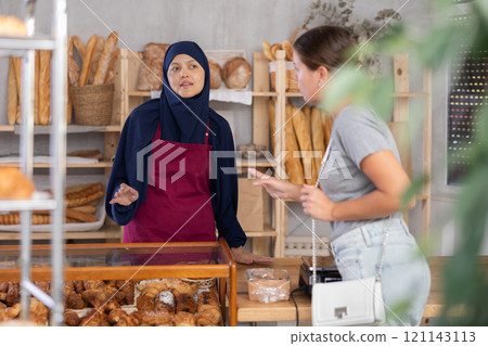 Muslim saleswoman speaks to girl in bakery 121143113