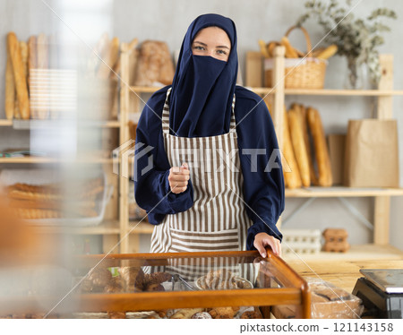 Polite Muslim female bakery owner welcoming customers 121143158