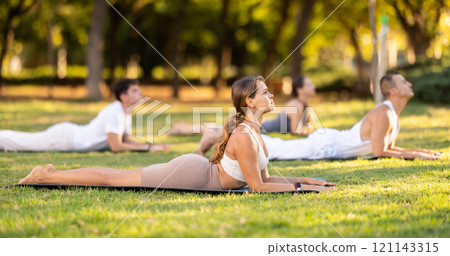 Yoga lesson visitors with coach perform dog face up and cobra pose in park 121143315