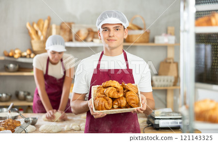 Successful young baker presenting golden croissants in inviting bakery Successful young baker presenting golden croissants in inviting bakery 121143325