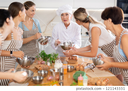 Elderly woman chef with bowl in hands tells women at culinary courses about traditions of cuisine Elderly woman chef with bowl in hands tells women at culinary courses about traditions of cuisine 121143331
