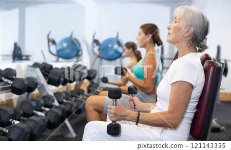 Mature sportswoman doing exercises with a barbell and dumbbells in gym 121143355