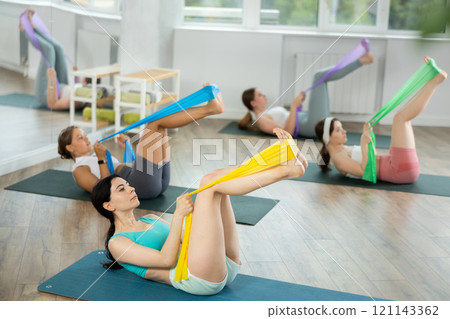 Girl lying and perform variety of exercises to strengthen muscles of press with wide resistance band 121143362