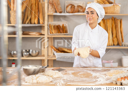 Young woman baker kneads the dough in bakery 121143363