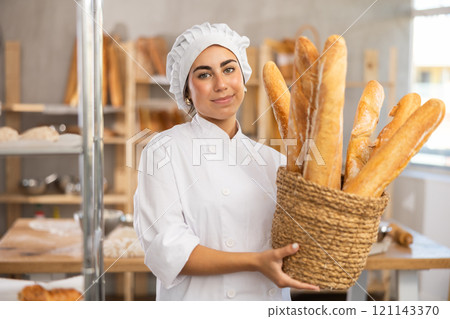 Young female baker with basket of baguettes 121143370