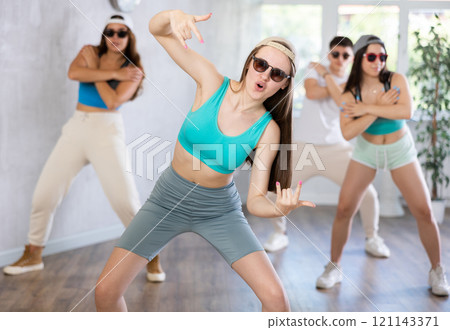Teenage girl practicing energetic dance movements with group of teens in choreography class 121143371