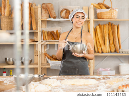 Young female baker whisking dough in bowl Young female baker whisking dough in bowl 121143383