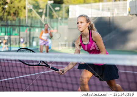 Sportive woman in shorts and t-shirt playing tennis on court. View through tennis net 121143389