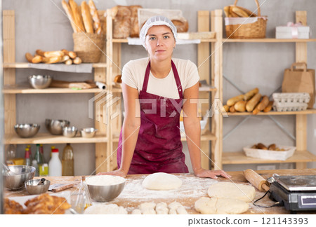 Young baker girl is standing near work table in kitchen, working with dough Young baker girl is standing near work table in kitchen, working with dough 121143393