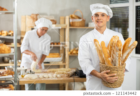 Happy male baker posing with basket of freshly baked baguettes in bakery, demonstrating concept of food industry and baker profession Happy male baker posing with basket of freshly baked baguettes in bakery, demonstrating concept of food industry and baker profession 121143442
