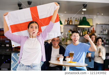 Enthusiastic company of young adult sports fans waving flag of England and supporting national team with beer in pub 121143492