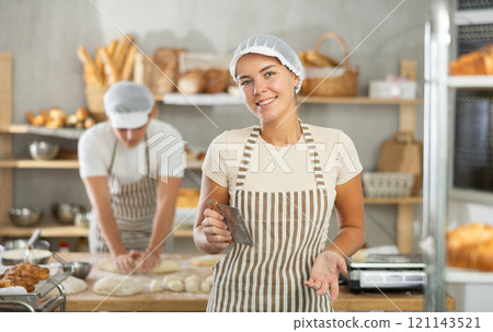 Young baker girl is standing near work table in kitchen, working with dough 121143521