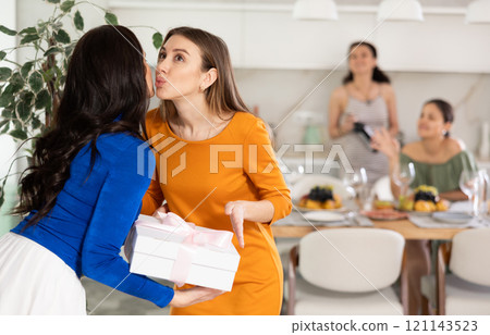 Woman joyfully greets her girlfriends on the doorstep, hugging and kissing each other Woman joyfully greets her girlfriends on the doorstep, hugging and kissing each other 121143523