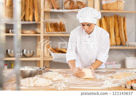Young female baker kneading dough on table 121143637