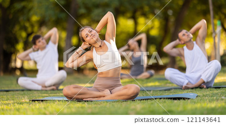 Girl performing stretches in lotus position during group yoga outdoors Girl performing stretches in lotus position during group yoga outdoors 121143641