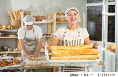Young woman are standing in kitchen with basket of finished products baguettes Young woman are standing in kitchen with basket of finished products baguettes 121143786