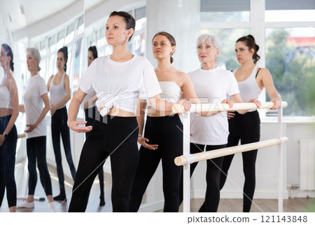 Woman practicing battement tendu at barre during group ballet class 121143848