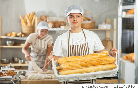 Young male baker holding baguettes in wicker basket 121143910