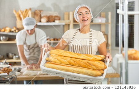 Happy female baker posing with basket of freshly baked baguettes in bakery, demonstrating concept of food industry and baker profession Happy female baker posing with basket of freshly baked baguettes in bakery, demonstrating concept of food industry and baker profession 121143926