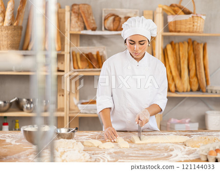 Young female baker cutting dough with scraper Young female baker cutting dough with scraper 121144033
