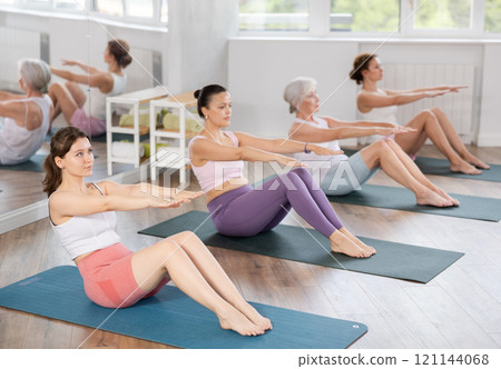 Athletic women doing pilates or aerobics - doing back exercises during group training in gym 121144068