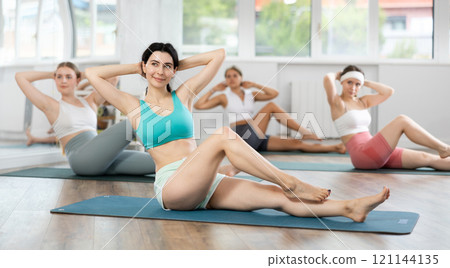 Young girls doing press exercise in sitting position in pilates studio Young girls doing press exercise in sitting position in pilates studio 121144135