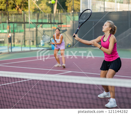 Sporty teenager girl player hitting ball with racket during friendly doubles couple match 121144282