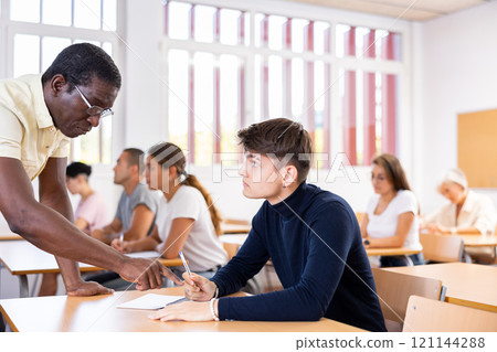 African American teacher helping student solve task during lesson 121144288