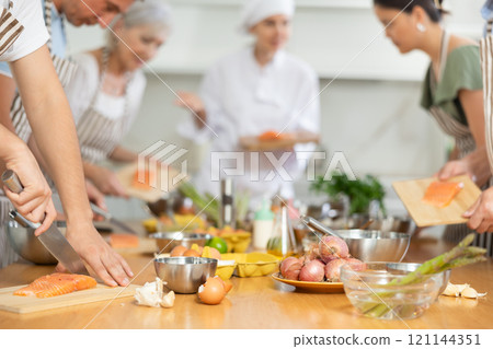 Pleased young man learner of culinary classes cutting piece of salmon 121144351
