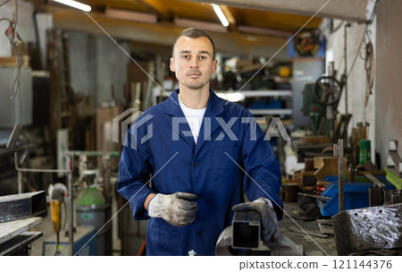 Male welder standing with a welding semi-automatic machine and a safety helmet in metal machining workshop Male welder standing with a welding semi-automatic machine and a safety helmet in metal machining workshop 121144376