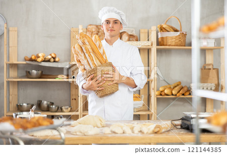 Happy male baker posing with basket of freshly baked baguettes in bakery, demonstrating concept of food industry and baker profession 121144385