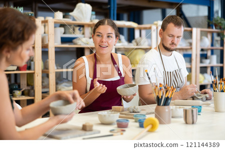 Three students in pottery workshop learn to create homemade plates and other utensils Three students in pottery workshop learn to create homemade plates and other utensils 121144389