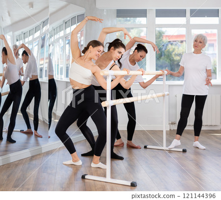 Young woman performing demi plie with cambre at barre in ballet class 121144396