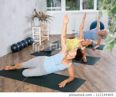 Old woman practicing side plank pose of yoga in training room during fitness classes Old woman practicing side plank pose of yoga in training room during fitness classes 121144409