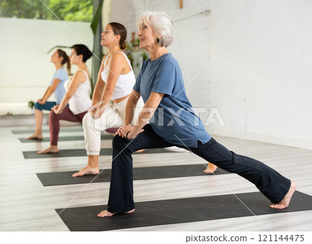 Mature female lunging in the middle of yoga class 121144475